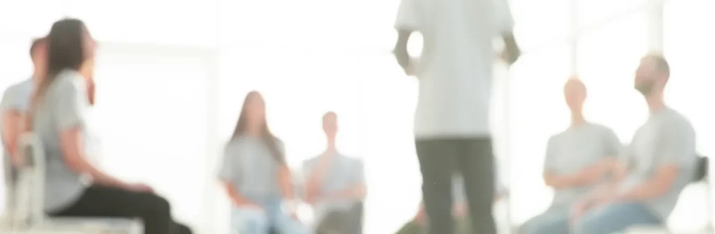 Ein Mann steht vor einer Lerngruppe im Stuhlkreis und unterrichtet.