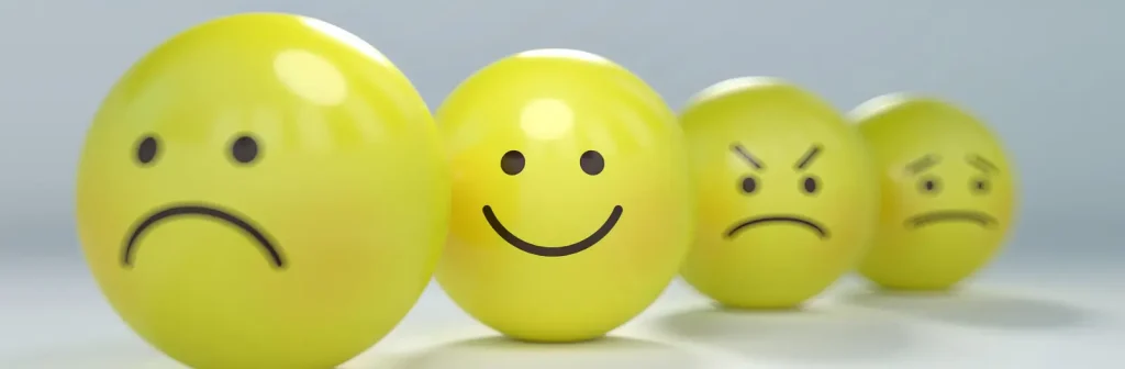 Positive Psychologie Gelbe Kugeln mit aufgemalten Gesichtern liegen nebeneinander. Der Focus liegt auf dem lachenden Smiley.